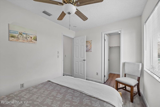 bedroom with ceiling fan, a spacious closet, a textured ceiling, a closet, and hardwood / wood-style flooring