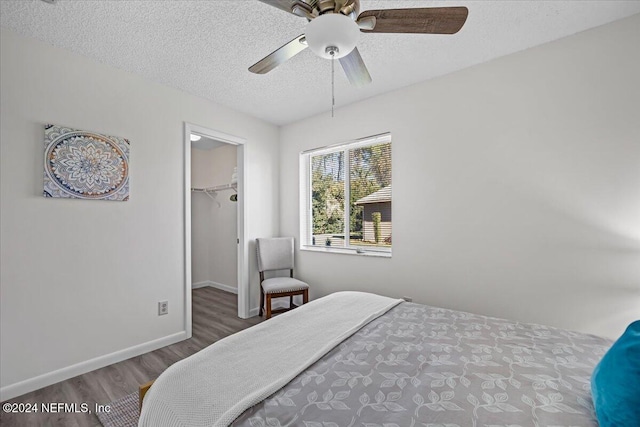 bedroom featuring ceiling fan, a spacious closet, a textured ceiling, dark hardwood / wood-style flooring, and a closet