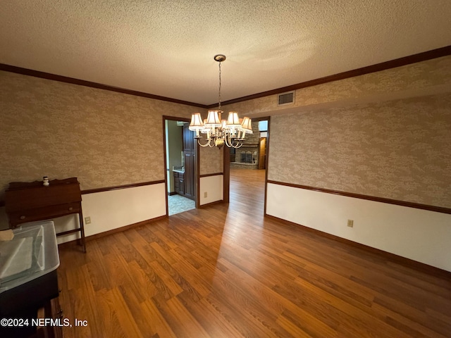 unfurnished dining area featuring a chandelier, a textured ceiling, crown molding, and dark wood-type flooring