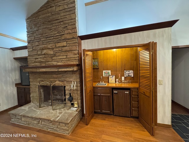 bar featuring dishwashing machine, light wood-type flooring, a stone fireplace, and sink