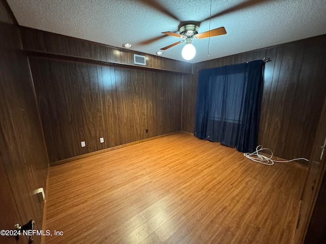 spare room with hardwood / wood-style flooring, ceiling fan, wood walls, and a textured ceiling