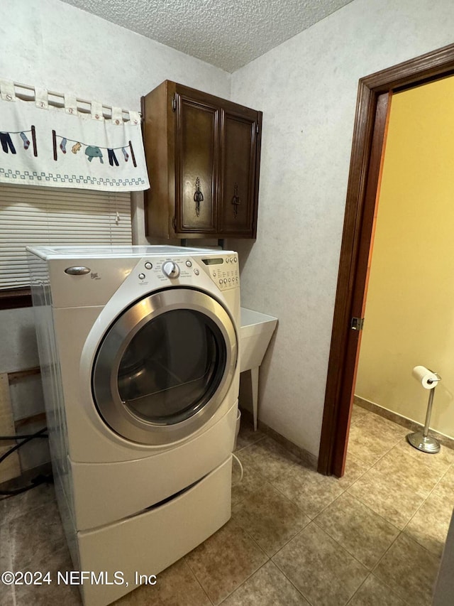 laundry room with light tile patterned floors, cabinets, a textured ceiling, and washer / dryer