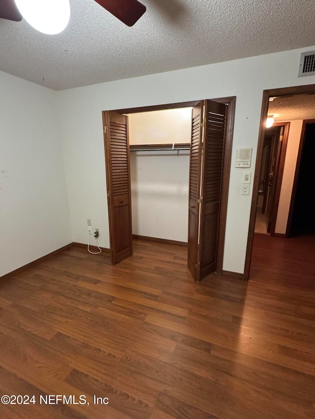 unfurnished bedroom featuring a textured ceiling, ceiling fan, dark wood-type flooring, and a closet