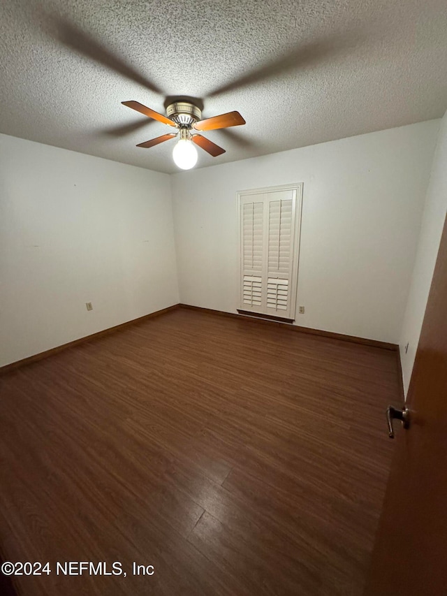 empty room with ceiling fan, dark wood-type flooring, and a textured ceiling