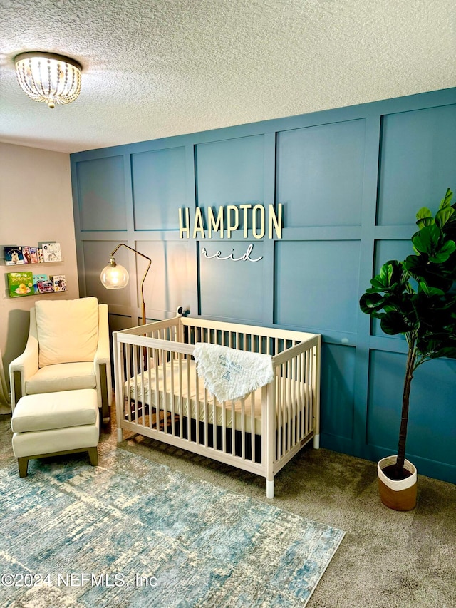 carpeted bedroom with a textured ceiling and a nursery area