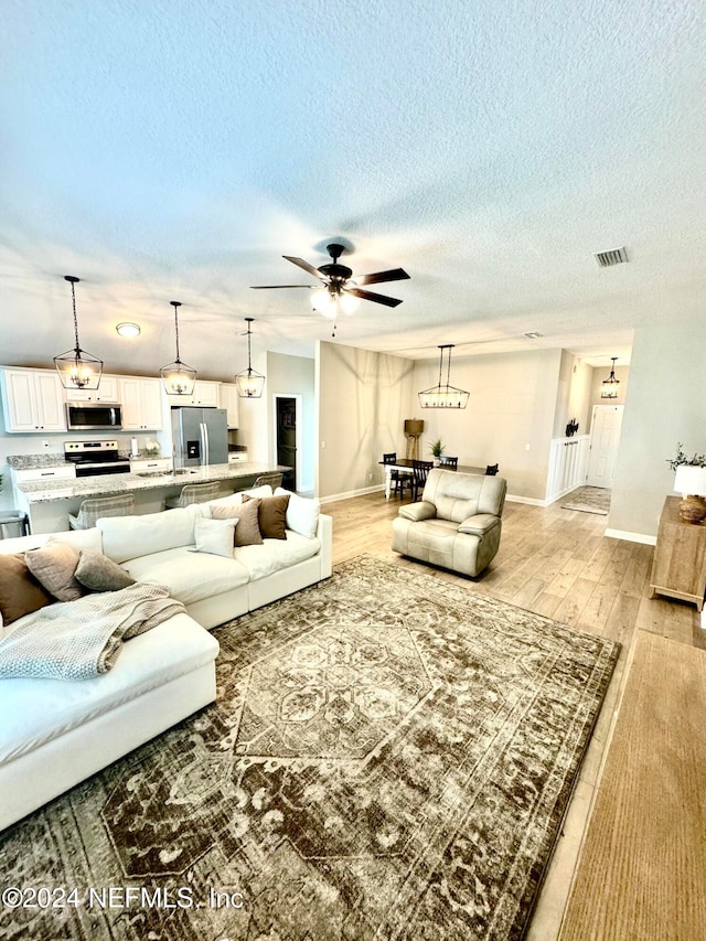 living room with a textured ceiling, light hardwood / wood-style flooring, and ceiling fan