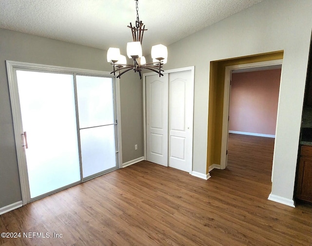 unfurnished dining area with lofted ceiling, wood-type flooring, a textured ceiling, and a notable chandelier