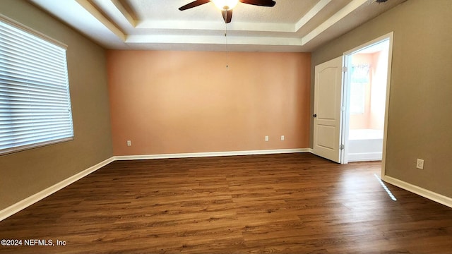 empty room featuring a tray ceiling, ceiling fan, and dark hardwood / wood-style flooring