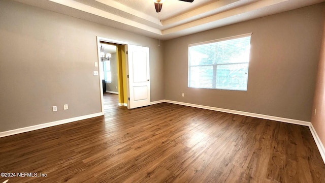 spare room with a raised ceiling, ceiling fan, and dark wood-type flooring