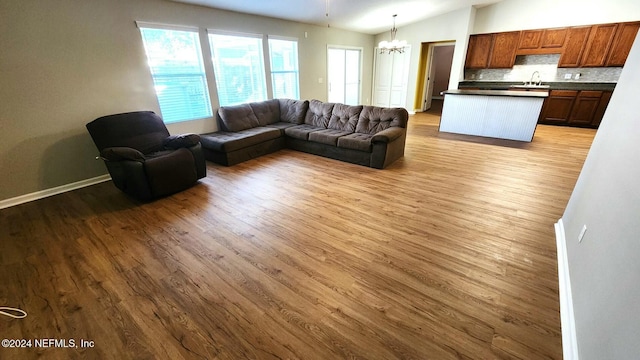 living room featuring sink, light hardwood / wood-style floors, vaulted ceiling, and an inviting chandelier