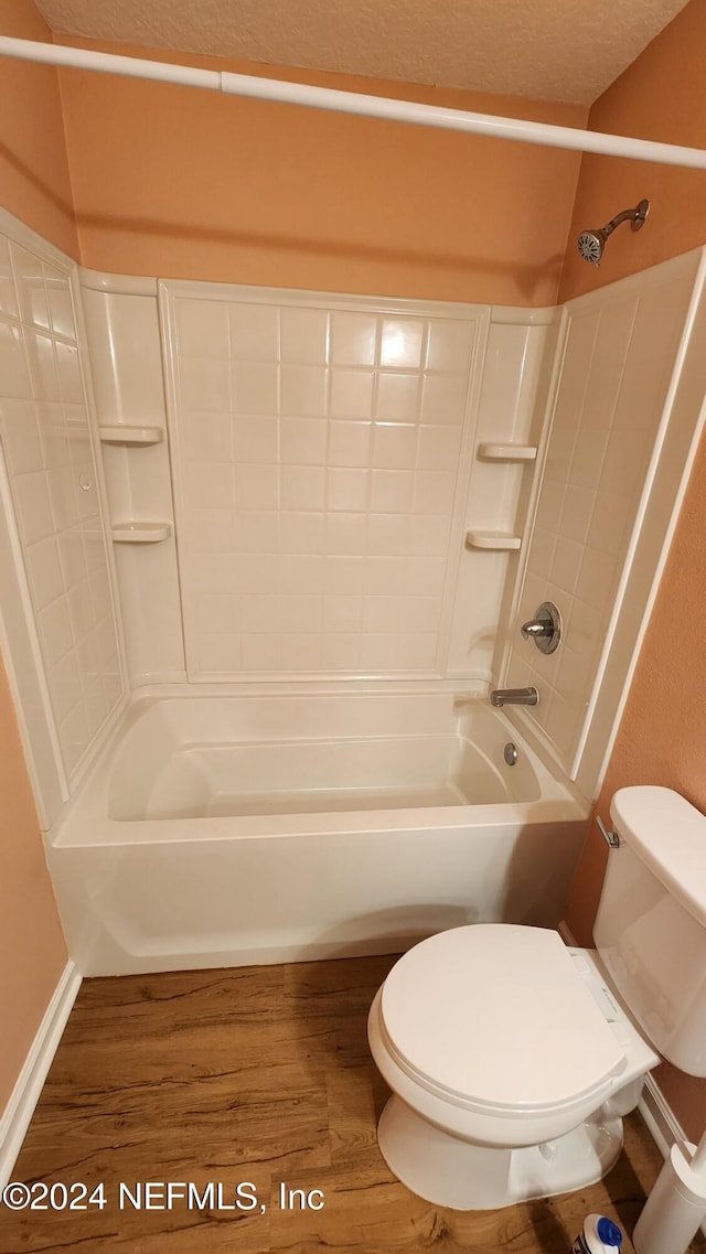 bathroom with toilet, washtub / shower combination, a textured ceiling, and hardwood / wood-style flooring