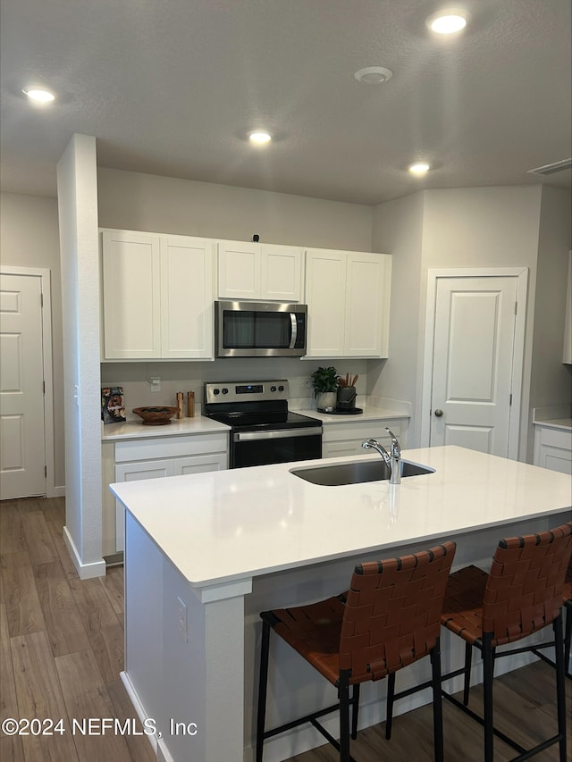 kitchen featuring stainless steel appliances, sink, light hardwood / wood-style floors, white cabinetry, and an island with sink