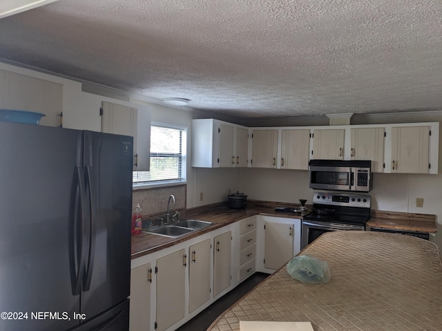 kitchen featuring appliances with stainless steel finishes, a textured ceiling, white cabinetry, and sink