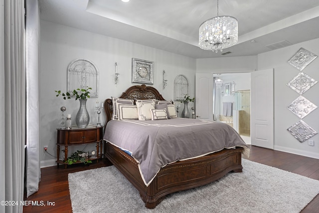 bedroom with a chandelier, dark hardwood / wood-style floors, a raised ceiling, and ensuite bathroom