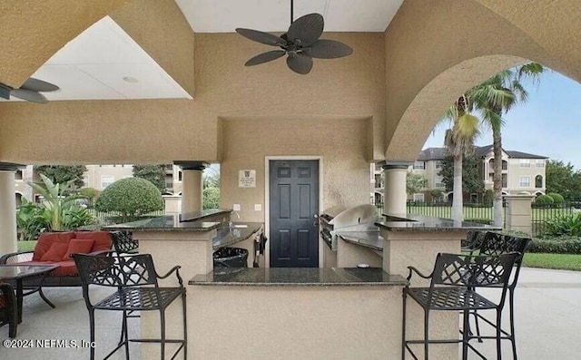 view of patio / terrace featuring grilling area, ceiling fan, an outdoor bar, and exterior kitchen