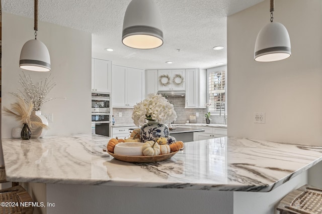 415 N Ocean Grande Dr Unit 101, Ponte Vedra Beach, FL 32082 - kitchen featuring a textured ceiling, a peninsula, backsplash, double oven, and white cabinetry
