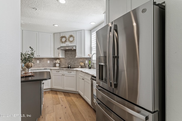 415 N Ocean Grande Dr Unit 101, Ponte Vedra Beach, FL 32082 - kitchen featuring appliances with stainless steel finishes, a textured ceiling, light wood finished floors, tasteful backsplash, and white cabinetry