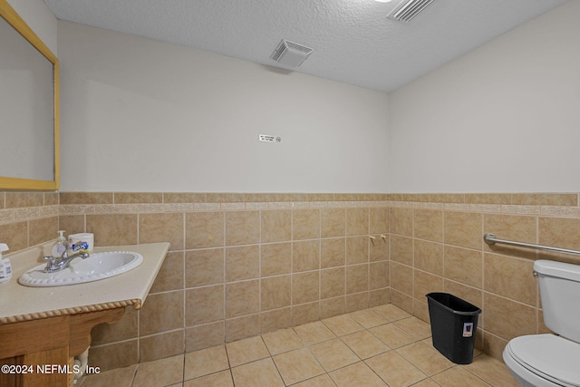 bathroom with tile patterned flooring, toilet, a textured ceiling, and tile walls