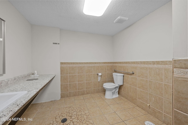 bathroom with tile patterned floors, a textured ceiling, toilet, and tile walls