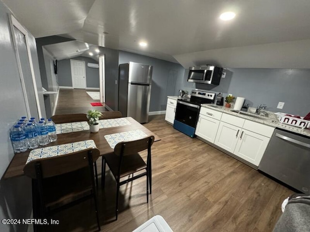 kitchen featuring white cabinetry, stainless steel appliances, vaulted ceiling, and hardwood / wood-style flooring