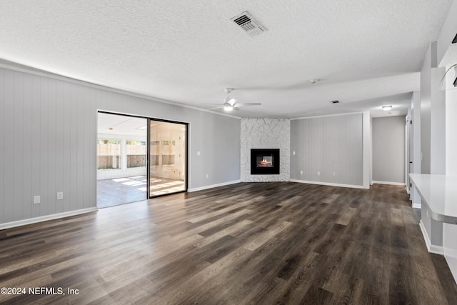 unfurnished living room with dark hardwood / wood-style floors, ceiling fan, a stone fireplace, and a textured ceiling