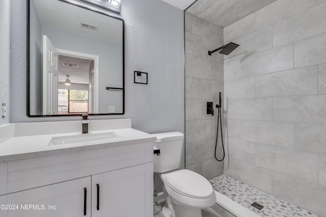 bathroom featuring tiled shower, vanity, a textured ceiling, and toilet