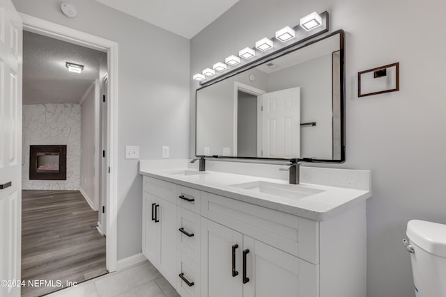 bathroom featuring a stone fireplace, hardwood / wood-style floors, a textured ceiling, toilet, and vanity