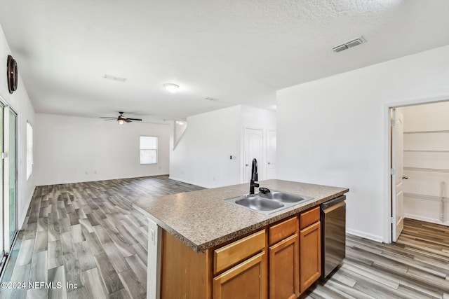 kitchen with a center island with sink, sink, light hardwood / wood-style flooring, stainless steel dishwasher, and ceiling fan