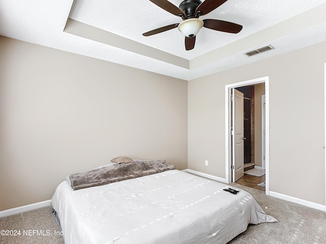 bedroom featuring a textured ceiling, light colored carpet, ensuite bath, and ceiling fan