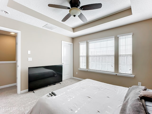 carpeted bedroom with a raised ceiling, ceiling fan, and a textured ceiling