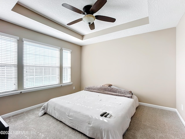 carpeted bedroom with a tray ceiling, ceiling fan, and a textured ceiling