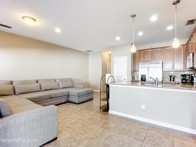 kitchen with light stone counters, sink, stainless steel appliances, and decorative light fixtures