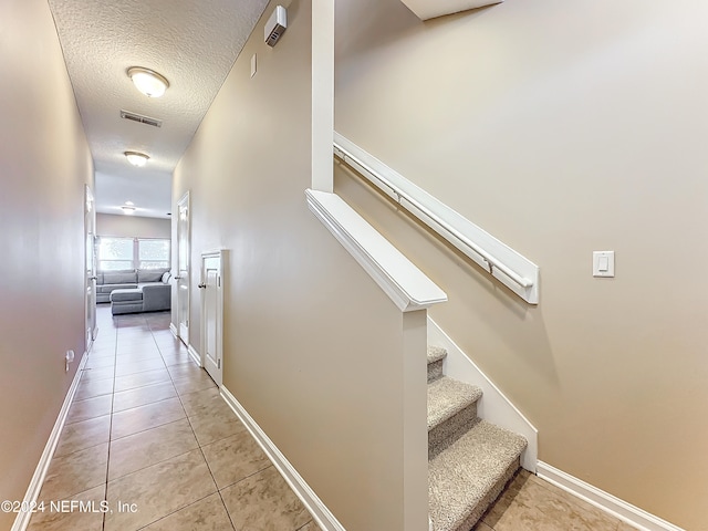 stairway with a textured ceiling and tile patterned floors