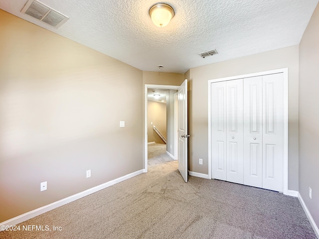 unfurnished bedroom with a textured ceiling, light carpet, and a closet