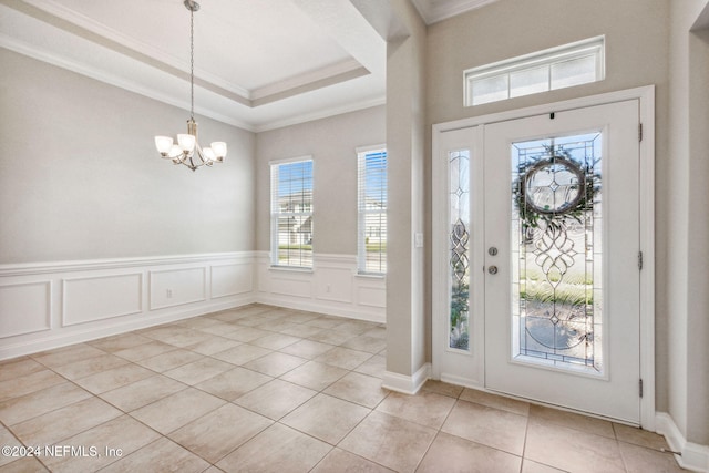 foyer entrance with a tray ceiling, an inviting chandelier, crown molding, and light tile patterned flooring