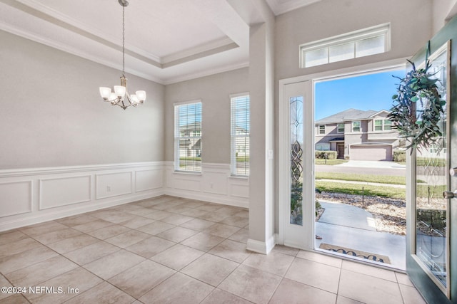 entrance foyer with a raised ceiling, light tile patterned floors, ornamental molding, and a chandelier