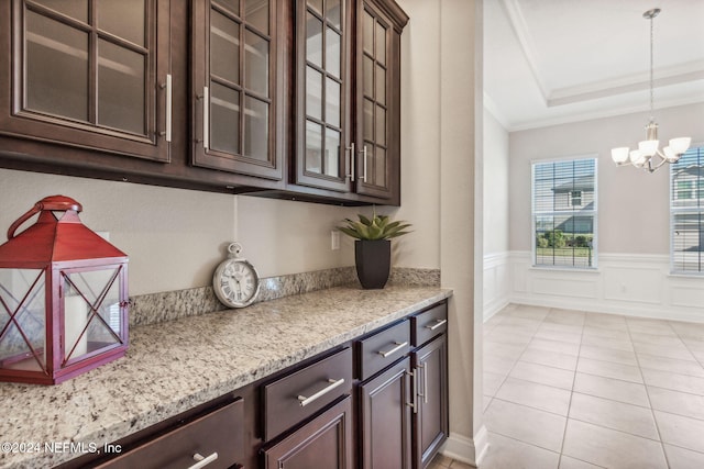 interior space featuring light stone countertops, ornamental molding, dark brown cabinetry, pendant lighting, and a notable chandelier