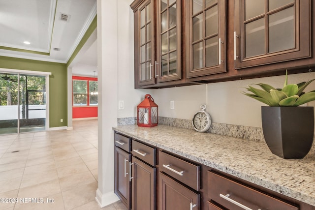 bar with dark brown cabinetry, light stone countertops, light tile patterned floors, and ornamental molding