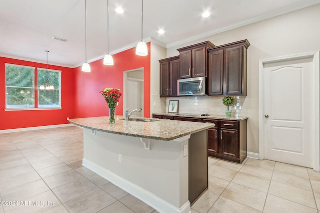 kitchen with a kitchen bar, light stone counters, a kitchen island with sink, sink, and pendant lighting