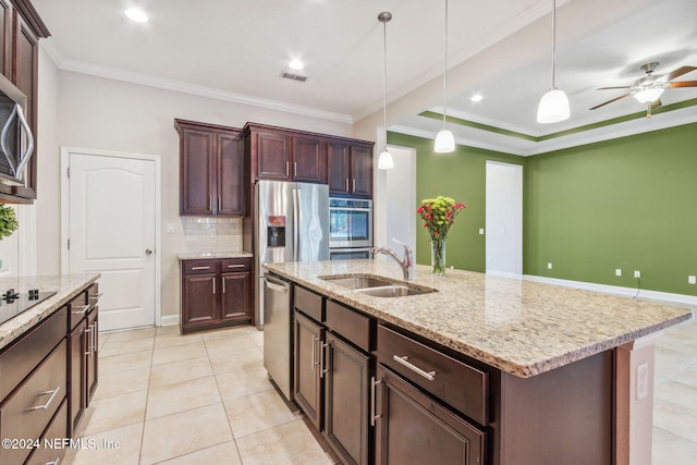 kitchen featuring stainless steel appliances, crown molding, sink, decorative light fixtures, and a center island with sink