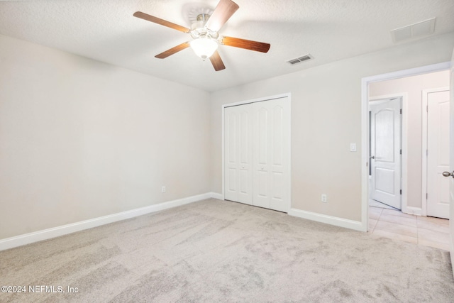 unfurnished bedroom featuring a textured ceiling, ceiling fan, light carpet, and a closet