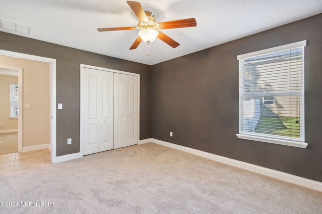 unfurnished bedroom with ceiling fan, a closet, light carpet, and a textured ceiling