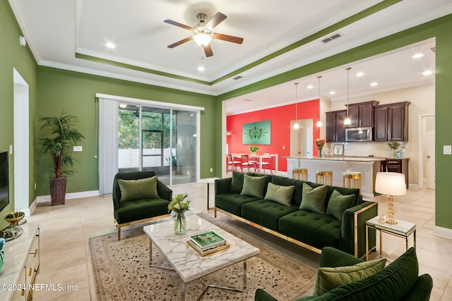 living room featuring ceiling fan, a raised ceiling, ornamental molding, and light tile patterned floors