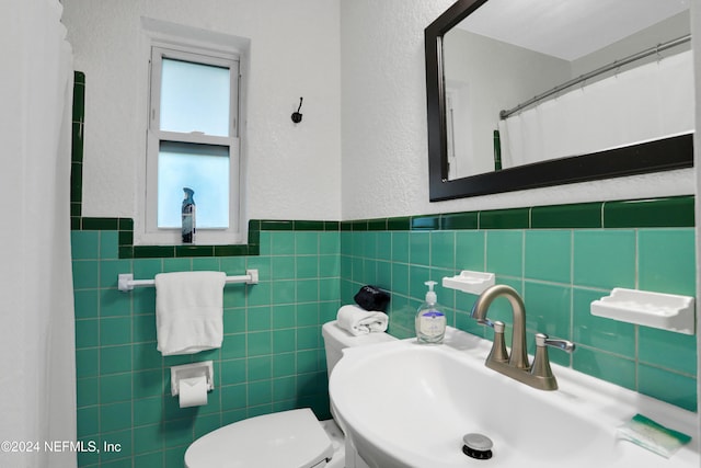 bathroom with toilet, sink, and tile walls