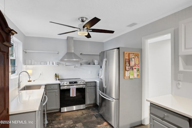 kitchen featuring ceiling fan, wall chimney exhaust hood, gray cabinets, appliances with stainless steel finishes, and ornamental molding