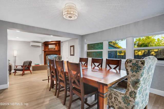 dining room with a wall mounted AC, light hardwood / wood-style flooring, a textured ceiling, and a notable chandelier