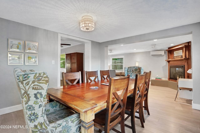 dining room with ceiling fan with notable chandelier, an AC wall unit, light hardwood / wood-style floors, a textured ceiling, and a large fireplace