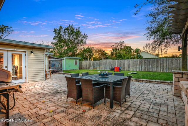 patio terrace at dusk featuring a storage unit and a lawn