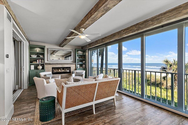 living room with a beach view, a water view, beamed ceiling, ceiling fan, and built in shelves