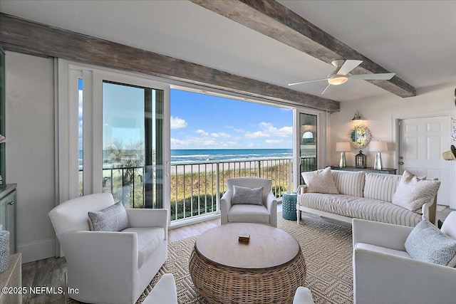 living room with a beach view, wood-type flooring, ceiling fan, beamed ceiling, and a water view